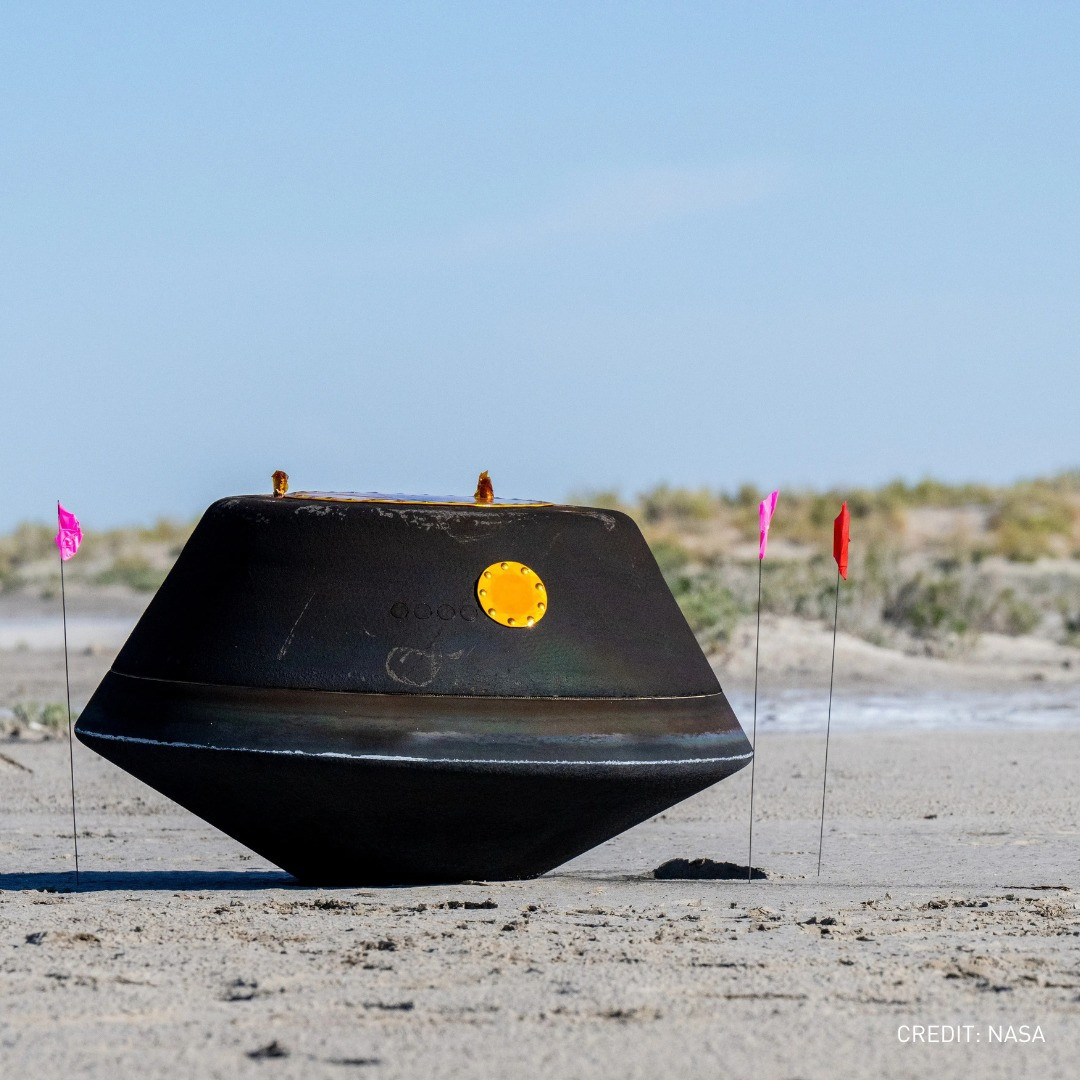 Metallic capsule on sandy beach with flags nearby.